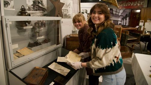 Two Minnesota State Mankato Department of Art and Design students posing while arranging an exhibit at the Blue Earth County Historical Society museum
