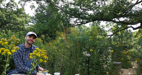 Matthew Kaproth sitting outside in a garden by yellow flowers