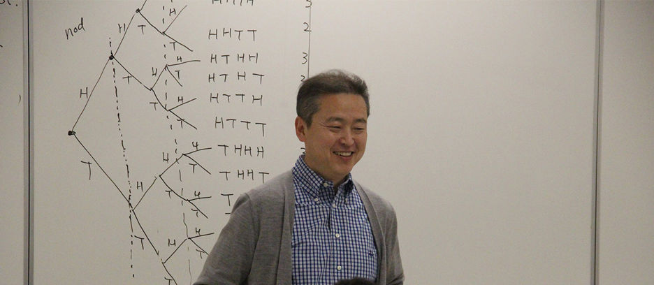 A male Economics professor standing in front of the classroom giving a lecture 