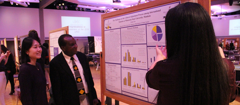 An Ethnic Studies student explaining her chart board to professors regarding the challenges on the cultural adjustment process among international students at Minnesota State University, Mankato