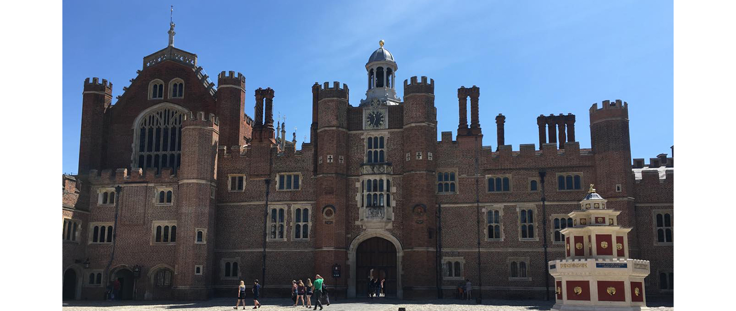 a large brick building with a clock on the top with Hampton Court Palace in the background