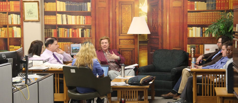Seven faculty members sitting on couches and chairs in a library having a discussion