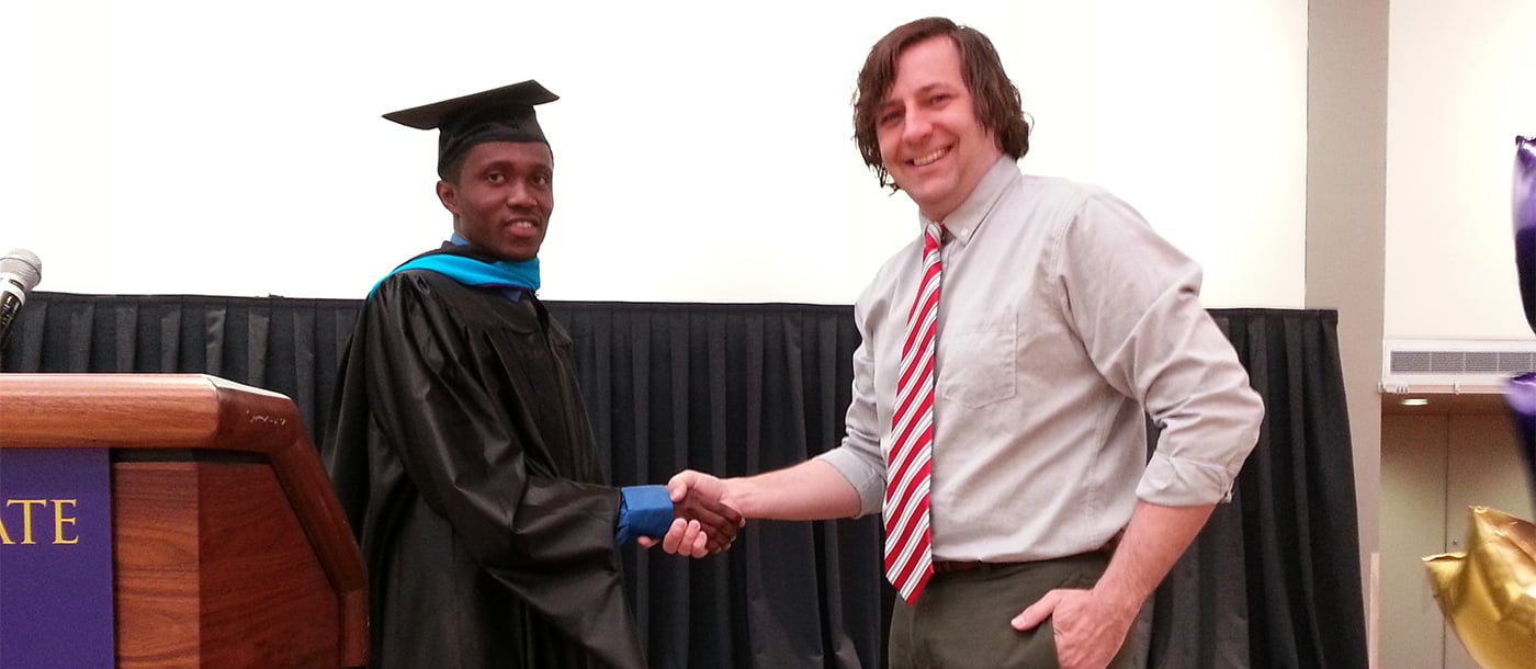 a male graduate shaking hands with a male professor